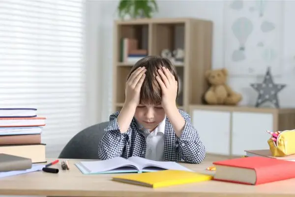 Kind sitzt verzweifelt bei den Hausaufgaben am Schreibtisch