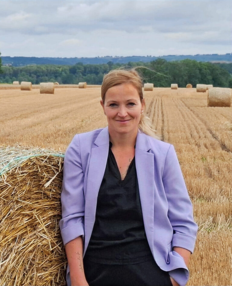 Frau in lila Jacke vor Strohballen auf einem Feld