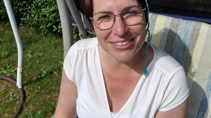 Lächelnde Frau sitzt draußen auf einem Stuhl